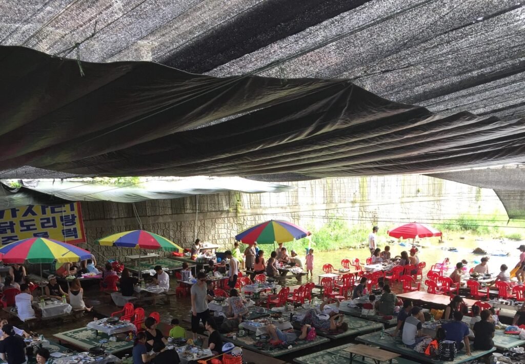 Korean valley restaurant with tables set in a cool mountain stream under umbrellas in summer